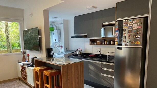 A modern kitchen with a central island, stainless steel appliances, and a large refrigerator. - Comfortable apartment with a view of nature (Porto Alegre)