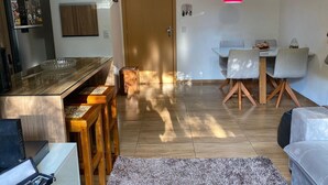 A modern kitchen with a wooden countertop and bar stools, a dining area with a table and chairs, and a red pendant light. - Comfortable apartment with a view of nature (Porto Alegre)