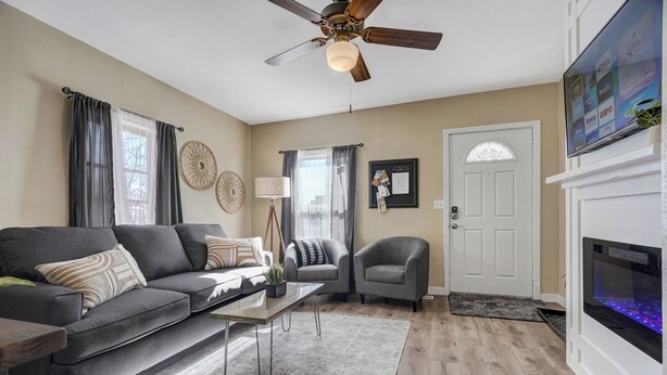 A living room with a sofa, armchairs, a coffee table, a fireplace, and a ceiling fan. - Downtown Urban Basecamp - Private Patio, Grill and Fireplace (Colorado Springs)