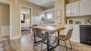 A kitchen with a wooden dining table, four chairs, and white cabinets. - Downtown Urban Basecamp - Private Patio, Grill and Fireplace (Colorado Springs)