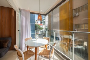 Een moderne kamer met een glazen balkon, een ronde eettafel, rieten stoelen en een grijze bank.