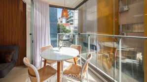 Une pièce moderne dotée d’un balcon en verre, d’une table à manger ronde, de chaises en osier et d’un canapé gris.