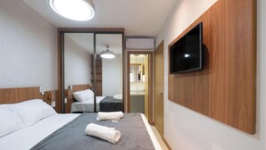 Une chambre d’hôtel avec un lit, un téléviseur fixé au mur, un miroir et un luminaire au plafond.