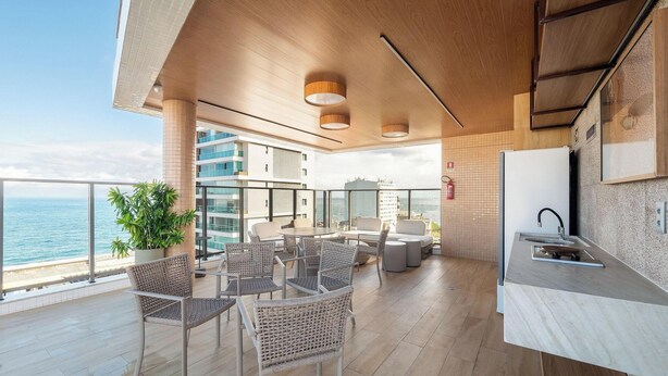 Une cuisine moderne avec vue sur la mer, des meubles en osier et un balcon agrémenté d’une plante.