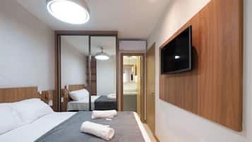 A hotel room with a bed, a flat-screen TV mounted on the wall, a ceiling light, and a sliding door leading to a bathroom.
