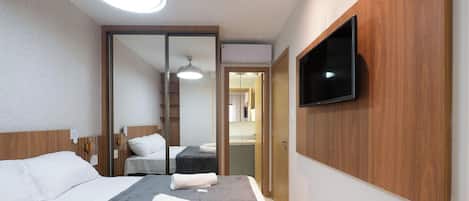 A hotel room with a bed, a flat-screen TV mounted on the wall, a ceiling light, and a sliding door leading to a bathroom.
