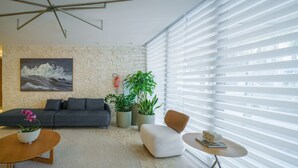 Un salon moderne avec un mur en pierre, un canapé gris, une table basse, une table d’appoint et une grande fenêtre avec des stores.