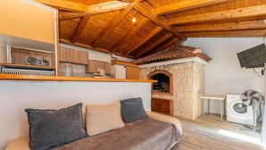 A cozy room with a wooden ceiling, a stone fireplace, a sofa with cushions, a washing machine, and a small table. - 2 bedroom awesome apartment in Pakostane (Pakostane)