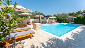 A poolside area with lounge chairs and umbrellas, a stone wall, and a clear blue pool. - 2 bedroom awesome apartment in Pakostane (Pakostane)