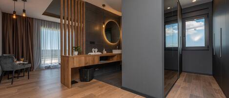 A modern bathroom with a wooden vanity, a round mirror, and a large window.