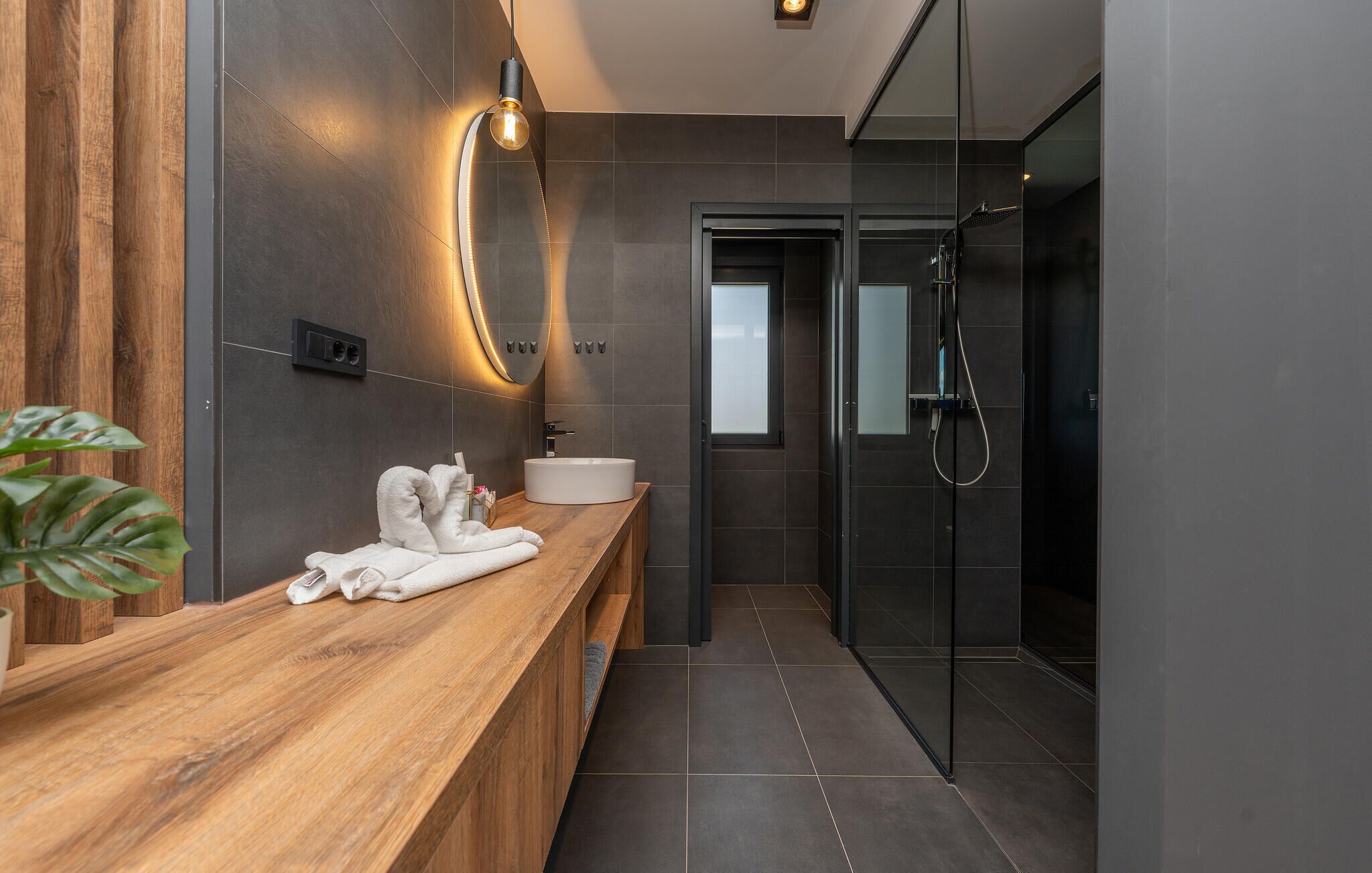A modern bathroom with a wooden vanity, a large mirror, a glass shower enclosure, and a white sink.