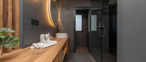 A modern bathroom with a wooden vanity, a large mirror, a glass shower enclosure, and a white sink.