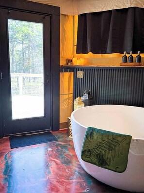 A room with a large bathtub, a door leading outside, and a window with a view of trees.