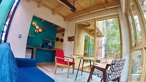 A room with a blue sofa, a red chair, a dining table with chairs, and a kitchen area with a blue wall and hexagonal decorations.