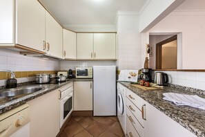 A compact kitchen with white cabinets, a built-in oven, a microwave, a refrigerator, and a coffee maker.