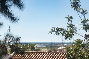 A view of a coastal area with terracotta roof tiles, a clear sky, and distant buildings.