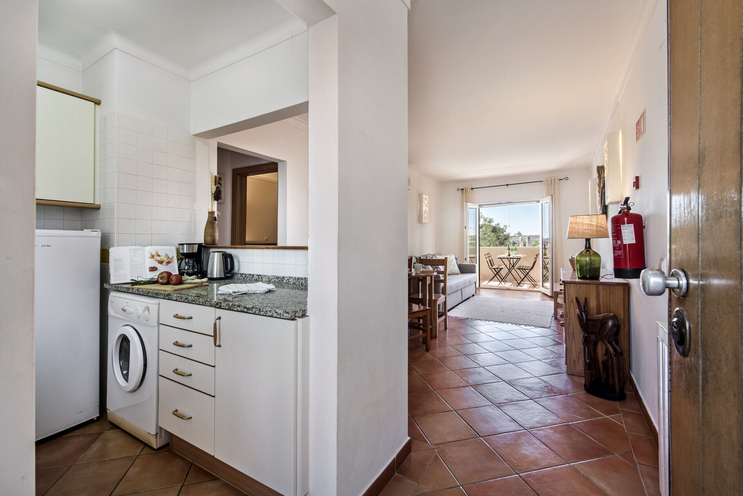 Uma cozinha com armários brancos, máquina de lavar e área de jantar com mesa e cadeiras.