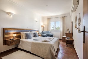 Ein Schlafzimmer mit einem großen Bett, Nachttischen, einem Sessel, einem Fenster mit Vorhängen und Wanddekoration.
