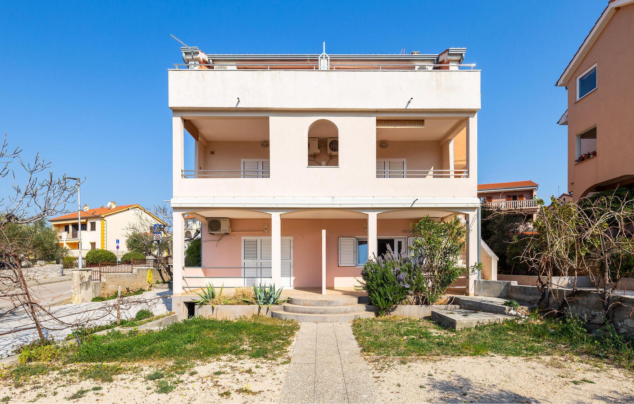 Un bâtiment à deux étages doté d’un balcon central, d’une entrée couverte et d’un petit jardin.
