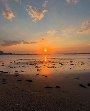 Une plage où l’on voit des empreintes de pas menant à l’eau, un coucher de soleil en arrière-plan et un ciel dégagé.