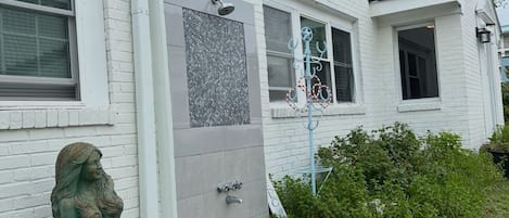Une maison blanche avec une porte grise, un petit jardin et une statue de sirène.