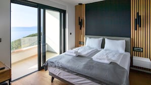 A modern bedroom with a large bed, a sliding glass door leading to a balcony with a scenic view, and a dark accent wall.