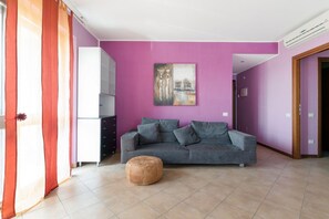 A living room with a grey sofa, a round ottoman, and a painting on the wall.