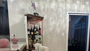 A bar area with a bar stool, a shelf with bottles, and a decorative plant.