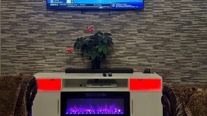 Un salon moderne avec un téléviseur à écran plat fixé à un mur texturé, une cheminée en dessous et un canapé agrémenté de coussins à motifs.