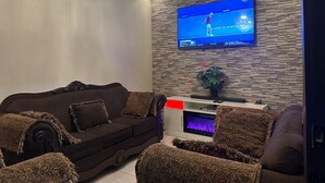 Un salon moderne doté d’un téléviseur à écran plat fixé sur un mur à texture, d’une cheminée et d’un lustre décoratif.