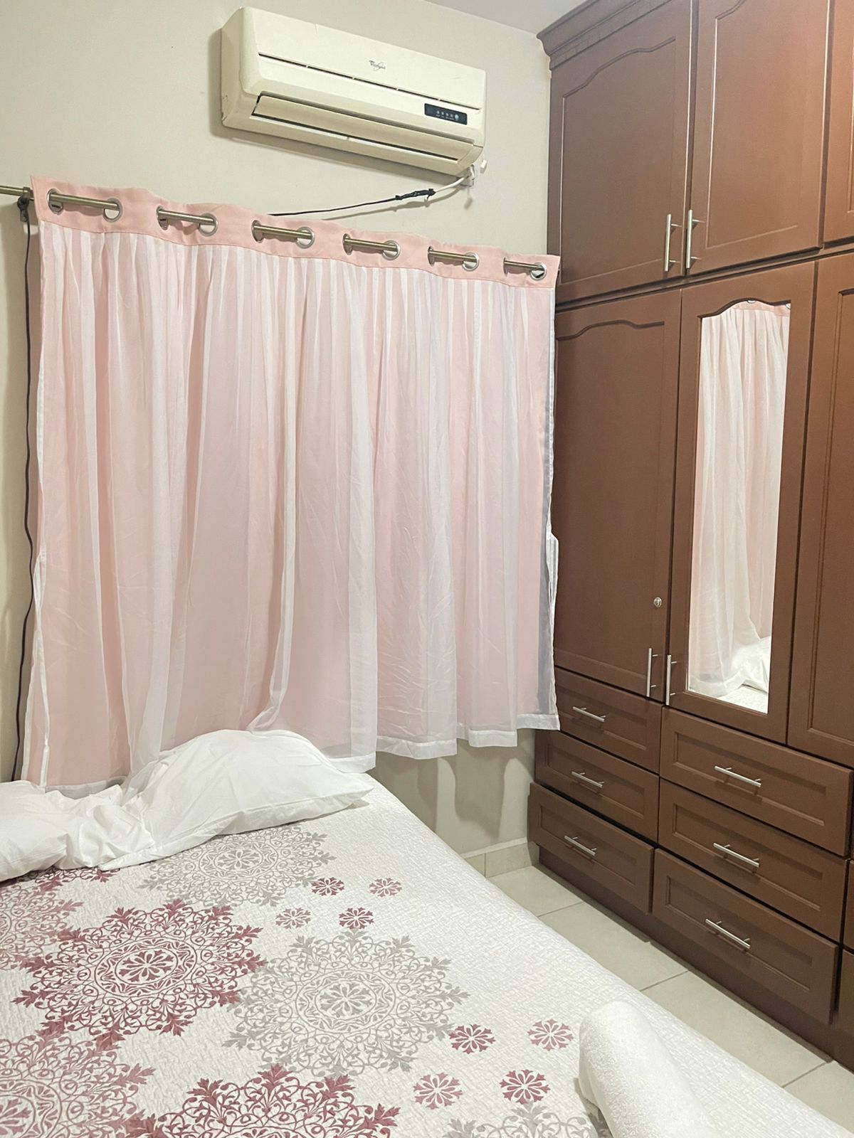 A bedroom with a bed, a wardrobe, and an air conditioning unit.