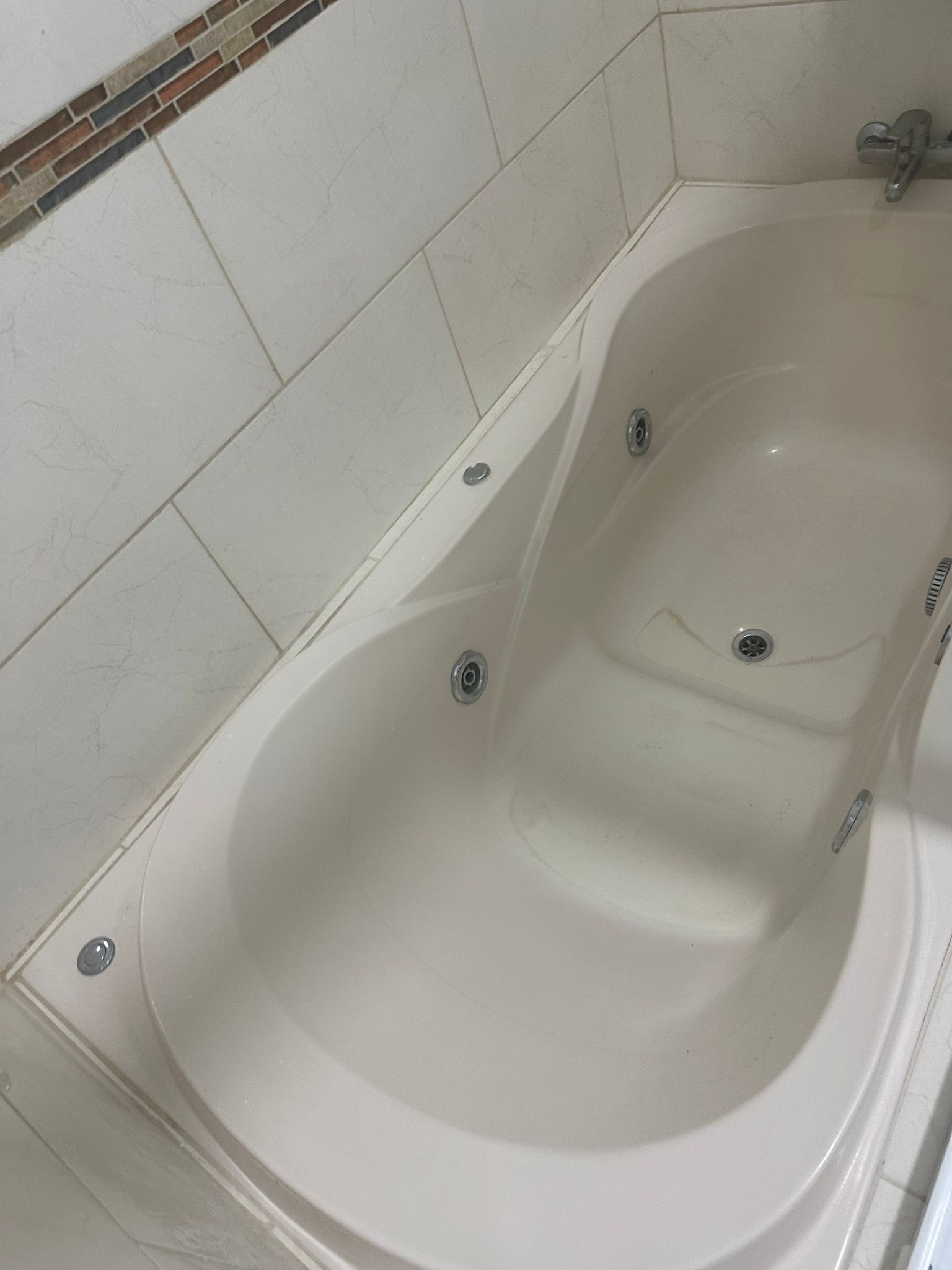 A white bathtub with two drain holes, set against a tiled wall with a brick pattern at the top.