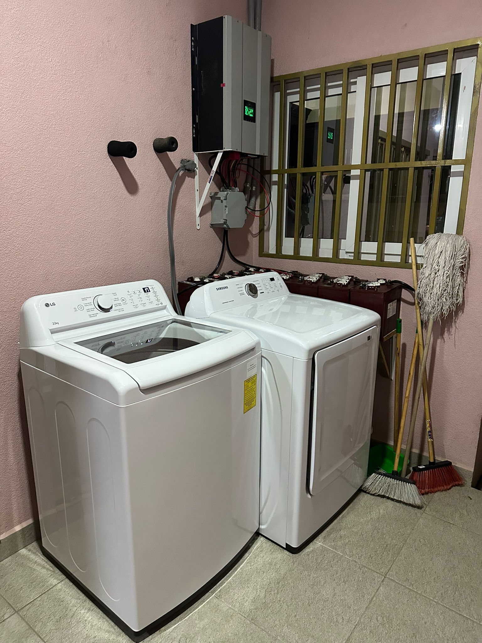 Une buanderie équipée de deux machines à laver à chargement frontal, d’une fenêtre grillagée et d’un balai appuyé contre le mur.