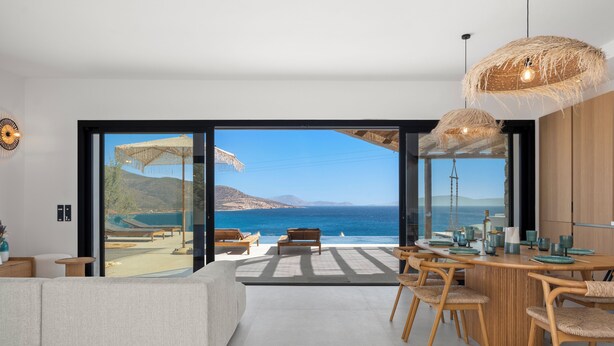Een moderne woonkamer met een grote glazen deur die uitkomt op een balkon met uitzicht op de zee.
