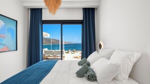 Een hotelkamer met een groot bed, uitzicht op zee en een balkon met buitenmeubilair.