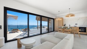 Een moderne woonkamer met een grote schuifglazen deur die uitkomt op een balkon met uitzicht op zee.
