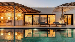 Een modern zwembadgedeelte met ligbedden, een stenen muur en een houten pergola.