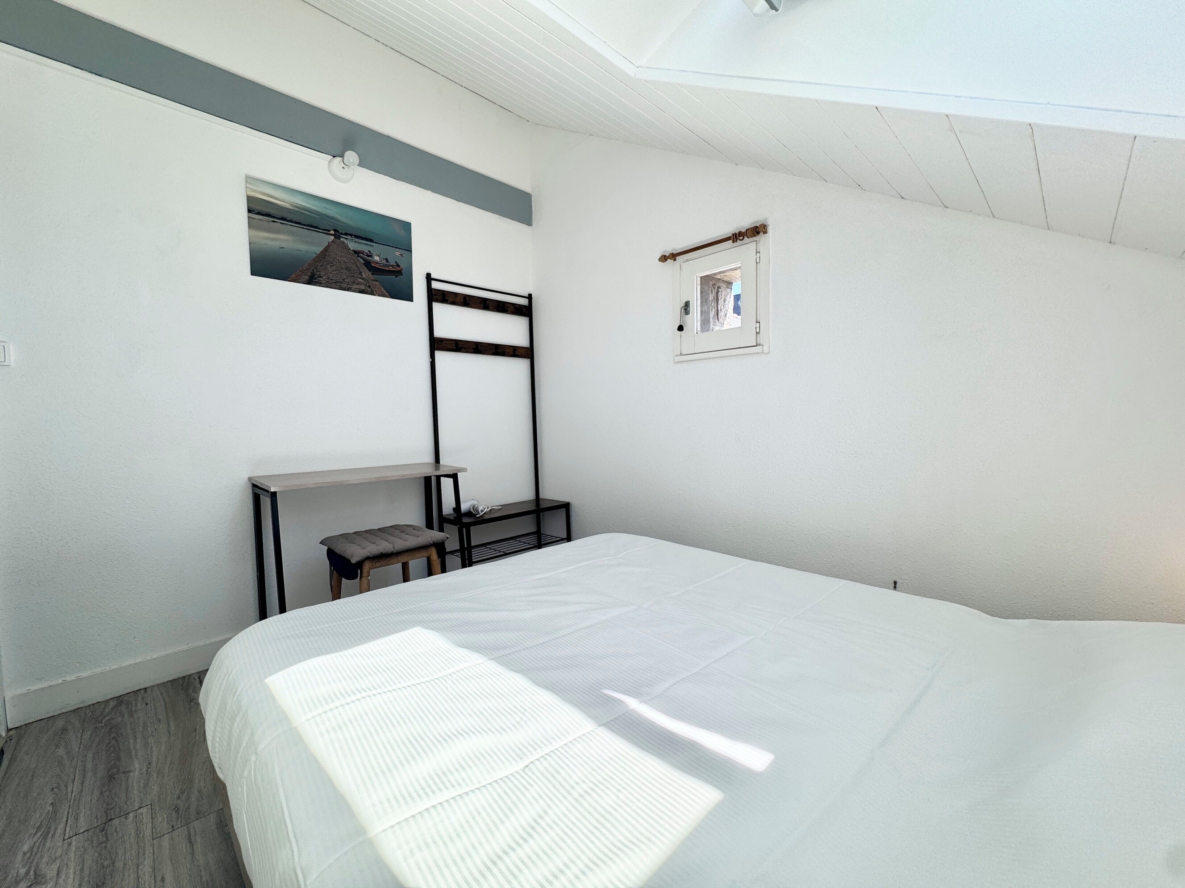 A bedroom with a bed, a desk, a chair, a ladder, and a small window.
