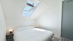 A bedroom with a skylight, a bed, bedside lamps, and a bench.