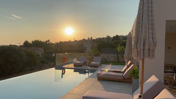 A rooftop pool area with lounge chairs and a sun umbrella, overlooking a residential neighborhood during sunset. - Luxurious Villa Retreat in Lourdata (Kefalonia)