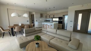 A modern living room with a sectional sofa, a dining area with a wooden table and chairs, and a kitchen with a central island and stainless steel appliances. - Luxurious Villa Retreat in Lourdata (Kefalonia)