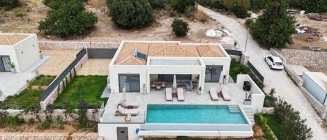 A modern two-story house with a swimming pool, outdoor seating, and a stone pathway.