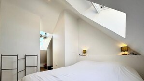 A bedroom with a large bed, skylight, and two wall-mounted lamps. - Maison refaite à neuf - Piscine et parking privé (Guidel)