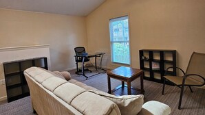 Een woonkamer met een beige bank, een kleine tafel, een stoel, een bureau en een plafondventilator.