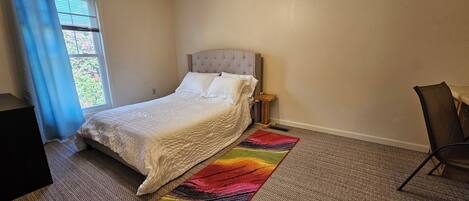 Une chambre à coucher avec un lit, un ventilateur de plafond, une fenêtre avec des rideaux, une table de chevet et une chaise.