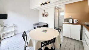 Un espacio habitable compacto con una mesa redonda de comedor, una kitchenette y un sofá gris.