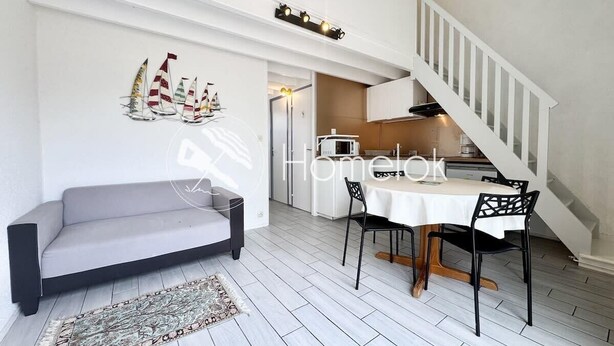 Una sala moderna con un sofá gris, una mesa de comedor con sillas negras y una escalera que sube a un nivel superior.