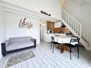 Un salon moderne avec un canapé gris, une table à manger entourée de chaises noires et un escalier menant à un niveau supérieur.