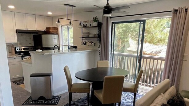 Een moderne keuken met witte kasten, een eethoek met een ronde tafel en stoelen, en een balkon met gordijnen.