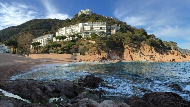 A coastal hotel with a rocky shoreline, a beach, and a hill with buildings. - 🏖Sea views + private beach. What else? (Tossa de Mar)